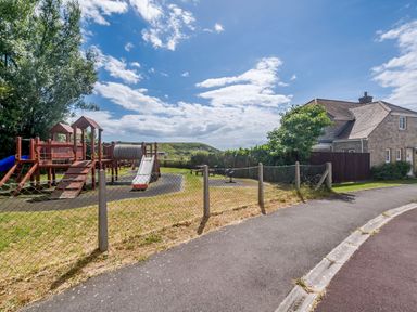 A playground with climbing structures and a slide next to a paved path and a house at West Bay Holiday Home in West Bay