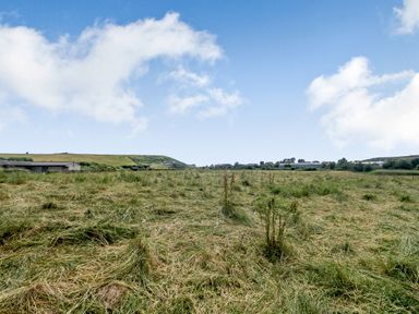 An open field with grass and some buildings in the distance under a partly cloudy sky at West Bay Holiday Home in West Bay