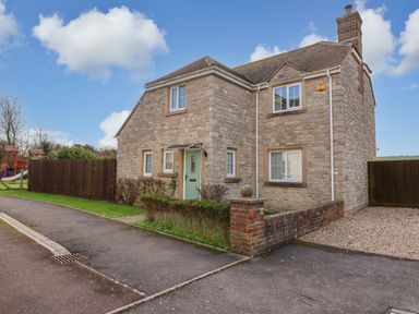 A stone house with a green front door and multiple windows next to a paved sidewalk at West Bay Holiday Home in West Bay