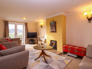 A living room with sofas a round table a TV on a stand a fireplace and a red plaid bench at West Bay Holiday Home in West Bay