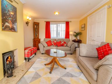 A living room with beige sofas red cushions a glass coffee table a fireplace and red curtains at West Bay Holiday Home in West Bay