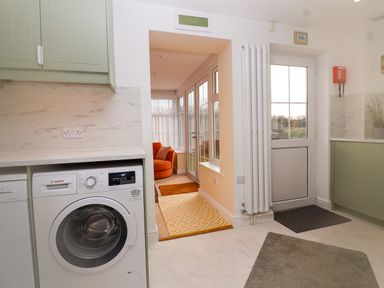A kitchen area with a washing machine a doorway leading to a small sunroom with an orange chair and rugs at West Bay Holiday Home in West Bay