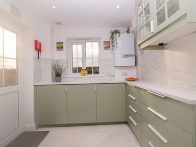 A kitchen with green cabinets a window a white countertop and a white boiler at West Bay Holiday Home in West Bay