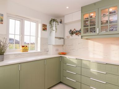 A kitchen with green cabinets white countertops a window and wall-mounted cupboards at West Bay Holiday Home in West Bay