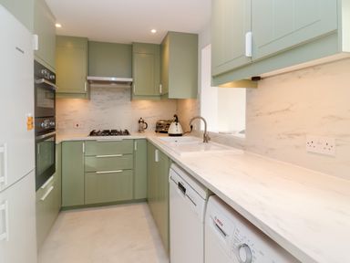 A kitchen with green cabinets white marble countertops a gas stove oven dishwasher washing machine and sink at West Bay Holiday Home in West Bay