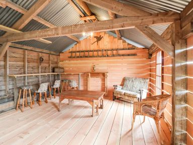 A wooden room with stools a table a loveseat and a wicker chair at Y Caban in Pontfadog near Llangollen