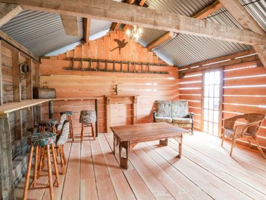 An attic room with wooden walls and floor bar stools a wooden table a small couch and a wicker chair at Y Caban Pontfadog near Llangollen