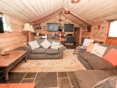 A living room with two gray sofas a wooden coffee table and a kitchen area with blue cabinets at Y Caban Pontfadog near Llangollen