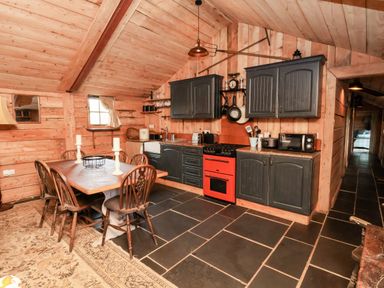 A kitchen with wooden walls and ceiling a dining table with chairs and a red oven at Y Caban Pontfadog near Llangollen