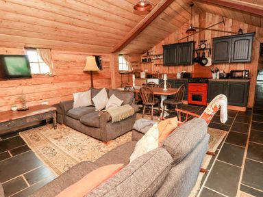 A living room with sofas dining table and kitchen cabinets in a wooden cabin at Y Caban in Pontfadog near Llangollen