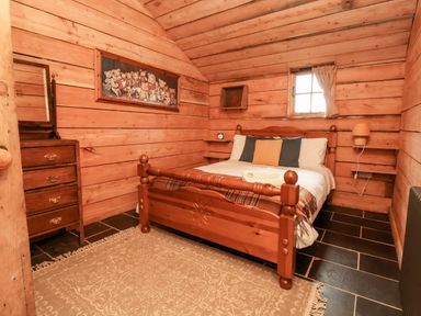 A bedroom with a wooden bed a chest of drawers and a rug at Y Caban Pontfadog near Llangollen