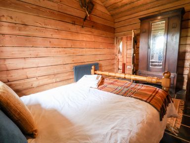 A bedroom with a wooden bed a white duvet an orange plaid blanket a wooden wardrobe and wooden walls at Y Caban Pontfadog near Llangollen