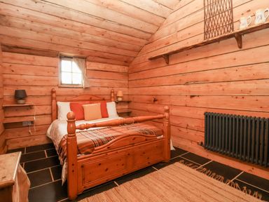 A bedroom with a wooden bed and plaid blanket in a wooden cabin at Y Caban in Pontfadog near Llangollen