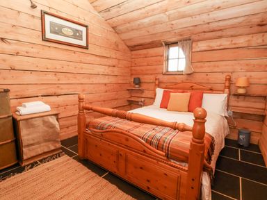 A bedroom with a wooden bed frame pillows and a blanket in a wooden cabin at Y Caban Pontfadog near Llangollen