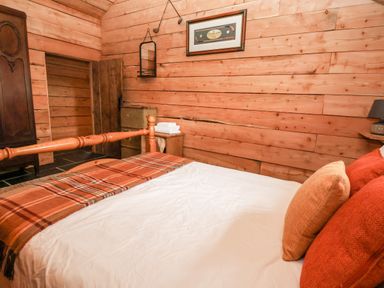 A bedroom with a wooden bed and plaid blanket in a wooden cabin at Y Caban Pontfadog near Llangollen