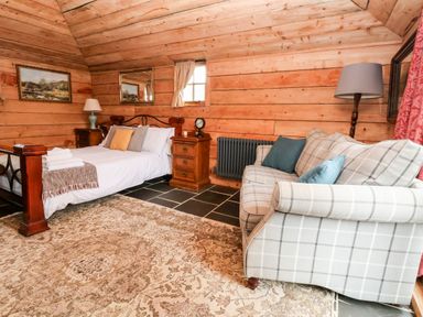 A bedroom with a bed a plaid sofa wooden walls and two bedside tables at Y Caban Pontfadog near Llangollen