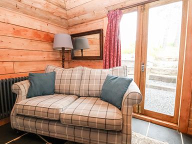 A corner of a room with a checkered sofa with two blue cushions a floor lamp a mirror red curtains and wooden double doors at Y Caban in Pontfadog near Llangollen