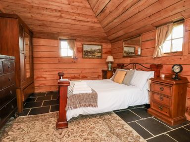 A bedroom with a wooden bed and nightstands with lamps curtains on windows and a rug on the floor at Y Caban Pontfadog near Llangollen