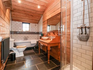 A bathroom with wooden walls a bathtub a toilet a shower and a wooden sink unit with a mirror at Y Caban Pontfadog near Llangollen