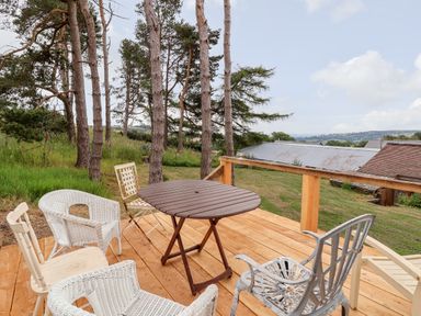 An outdoor wooden deck with various chairs and a small table overlooking trees and rooftops at Y Caban Pontfadog near Llangollen