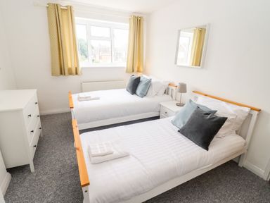 A bedroom with two single beds pillows and towels a chest of drawers and a window with yellow curtains at 17 Sands Close Broadway