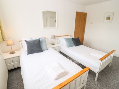 A bedroom with two single beds with pillows and towels bedside tables with lamps a wooden door and a wall mirror at 17 Sands Close in Broadway