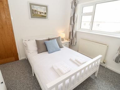 A bedroom with a white bed and pillows a bedside table with a lamp a window and a radiator at 17 Sands Close Broadway