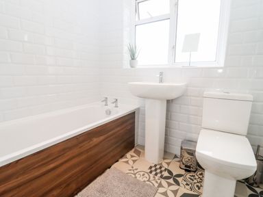 A bathroom with a bathtub a sink a toilet a small plant on the window sill and patterned floor tiles at 17 Sands Close in Broadway