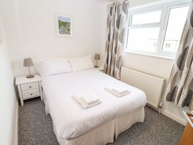 A bedroom with a double bed white bedding bedside tables lamps and a window with patterned curtains at 17 Sands Close Broadway