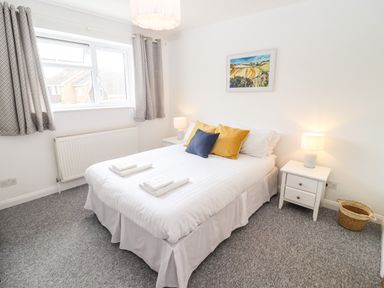 A bedroom with a double bed bedside tables lamps a window with curtains and a painting on the wall at 17 Sands Close in Broadway