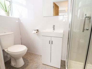 A bathroom with a toilet, sink with cabinet, shower enclosure, and a window with a plant at 17 Sands Close Broadway