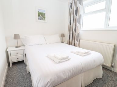 A bedroom with a double bed two bedside tables with lamps a window with curtains and a radiator at 17 Sands Close in Broadway