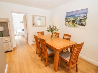 A dining room with a wooden table surrounded by six chairs and a vase of flowers on the table at 17 Sands Close in Broadway
