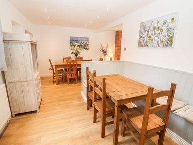 A dining area with two wooden tables and chairs a cabinet and flowers on the tables at 17 Sands Close in Broadway