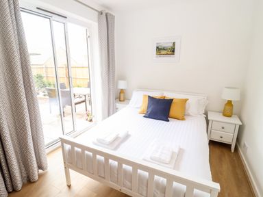 A bedroom with a white bed yellow and blue pillows bedside tables with lamps and sliding glass door at 17 Sands Close in Broadway