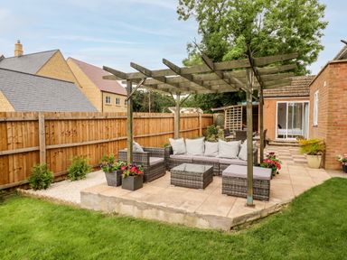 An outdoor patio with wicker furniture under a wooden pergola and a fenced lawn area at 17 Sands Close in Broadway