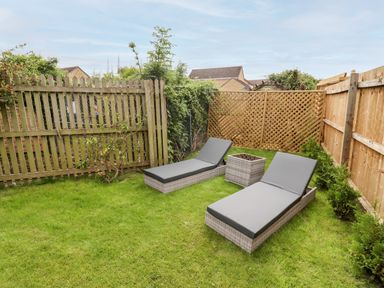 A small backyard with two grey cushioned lounge chairs and a square wicker table on grass at 17 Sands Close in Broadway