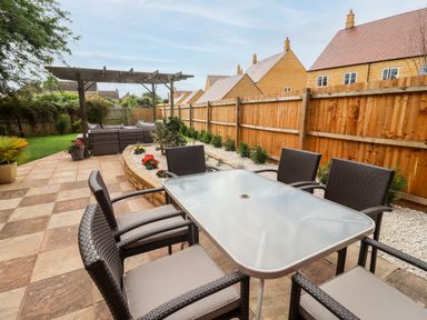 An outdoor patio with a glass table and wicker chairs next to a garden bed and wooden fence at 17 Sands Close in Broadway