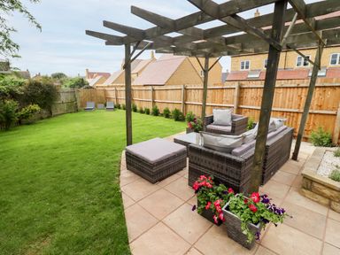 A garden with a wooden pergola covering outdoor wicker furniture and flowers at 17 Sands Close in Broadway