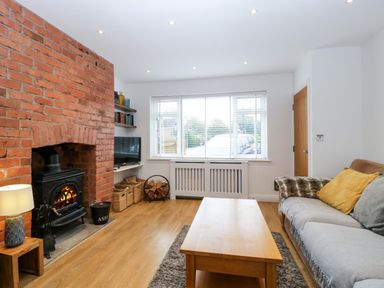 A living room with a brick fireplace a wooden coffee table and sofa with cushions at 17 Sands Close in Broadway