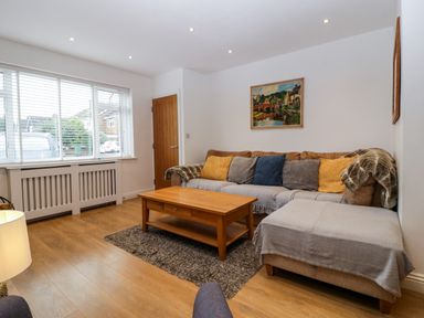 A living room with a sectional sofa with cushions a wooden coffee table a rug and a wall painting at 17 Sands Close in Broadway