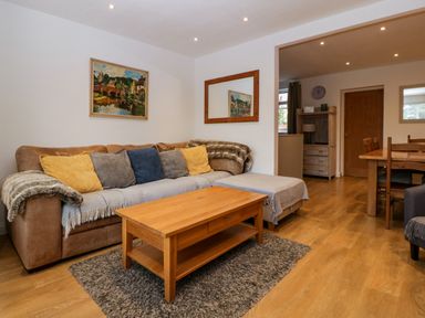 A living room with a sofa with cushions a wooden coffee table and a dining area at 17 Sands Close in Broadway