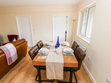 A dining table set for four with plates glasses and a blue bottle next to a brown leather sofa and windows at Caldey Lodge in Manorbier