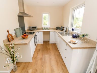A kitchen with wooden countertops white cabinets a stove a microwave a sink and a window at Caldey Lodge Bier Wood Lodges in Manorbier