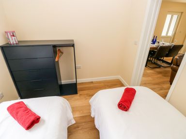 A bedroom with two single beds with red towels on each bed a black dresser with hangers and a view into a dining area at Caldey Lodge Bier Wood Lodges in Manorbier