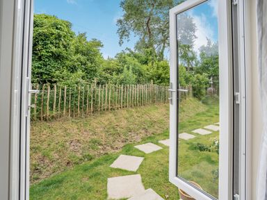 A garden with a stone path and a wooden fence viewed through open glass doors at Caldey Lodge Bier Wood Lodges in Manorbier