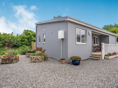 A gray wooden lodge with gravel ground and potted flowers at Caldey Lodge (Bier Wood Lodges) in Manorbier