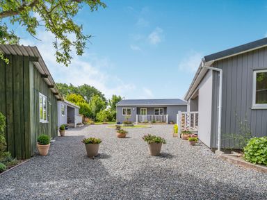An outdoor area with three gray buildings surrounded by potted plants and gravel at Caldey Lodge (Bier Wood Lodges) in Manorbier