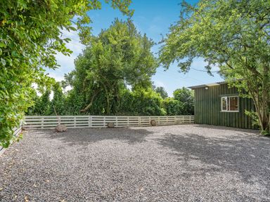 An outdoor area with gravel ground a green wooden shed white fence and trees at Caldey Lodge Bier Wood Lodges in Manorbier