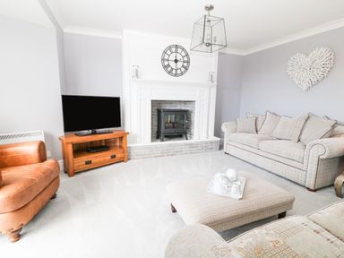 A living room with a television on a wooden stand a fireplace a beige sofa a brown armchair and a large ottoman at 12 Claremont Falls Polperro